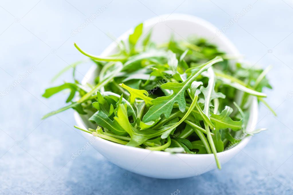 Fresh arugula leaves in bowl on table. Light background, closeup