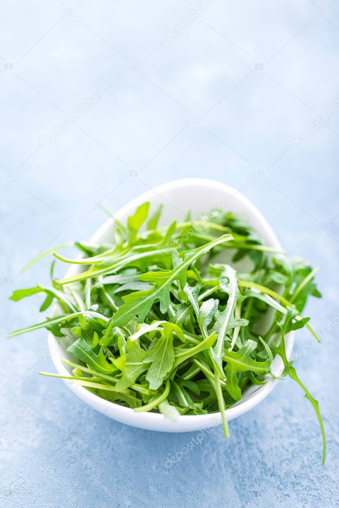 Fresh arugula leaves in bowl on table. Light background, closeup