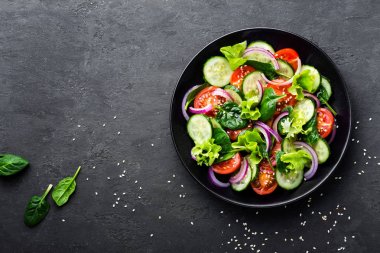 Taze domates, salatalık, soğan, ıspanak, marul ve susam plaka üzerinde sağlıklı sebze salatası. Diyet menüsü. Üstten Görünüm.