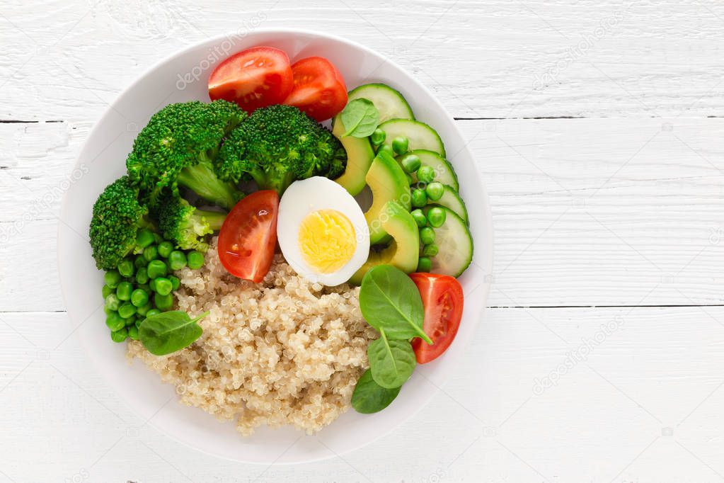Healthy detox dish with egg, avocado, quinoa, spinach, fresh tomato, green peas and broccoli on white wooden background, top view