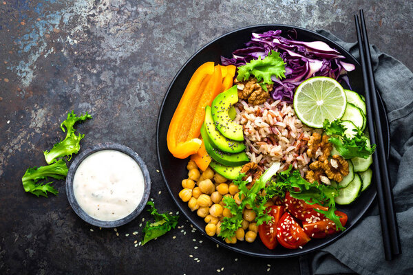 Buddha bowl dish with brown rice, avocado, pepper, tomato, cucumber, red cabbage, chickpea, fresh lettuce salad and walnuts. Healthy vegetarian eating, super food. Top view