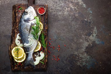 Taze malzemelerle ahşap tahta üzerinde yemek pişirmek için dorado balık. Ham çipura veya dorada balık karanlık vintage metal arka plan üzerinde. Diyet yiyecek. Üstten Görünüm