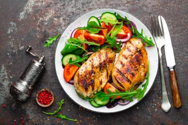 Izgara tavuk göğsü. Kızarmış tavuk fileto ve taze sebze salatası domates, salatalık ve roka yaprakları. Salatalı tavuk eti. Sağlıklı yiyecekler. Düz yatıyordu. Üst Manzara. Koyu arkaplan