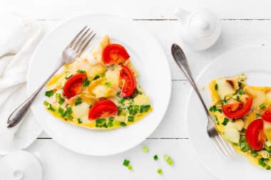 Omlet. Kızarmış yumurta. Yeşil soğan ve taze domates ile omlet. Kırmadan beyaz tabakta. Kahvaltı. Üstten Görünüm. Beyaz ahşap zemin