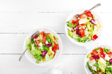 Taze yeşillik, marul, avokado, domates, seet biber ve keçi peyniri ile sağlıklı sebze salatası. Kahvaltı için lezzetli ve besleyici yiyecek çanak. Beyaz ahşap arka plan üzerinde salatası kaseler. Üstten Görünüm