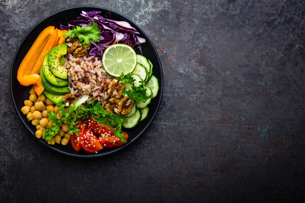 Buddha bowl dish with brown rice, avocado, pepper, tomato, cucumber, red cabbage, chickpea, fresh lettuce salad and walnuts. Healthy vegetarian eating, super food. Top view