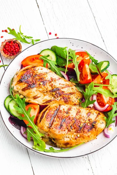 Grilled chicken breast. Fried chicken fillet and fresh vegetable salad of tomatoes, cucumbers and arugula leaves. Chicken meat salad. Healthy food. Flat lay. Top view. White background