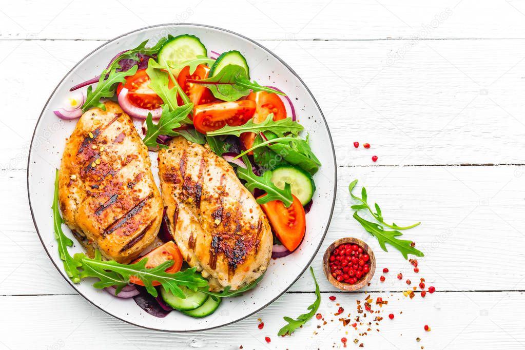 Grilled chicken breast. Fried chicken fillet and fresh vegetable salad of tomatoes, cucumbers and arugula leaves. Chicken meat salad. Healthy food. Flat lay. Top view. White background