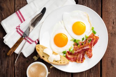 Kızarmış yumurta, pastırma ve İtalyan ciabatta ekmeği beyaz tabakta. Bir fincan kahve. Kahvaltı. Üstten Görünüm. Ahşap arka plan