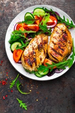 Izgara tavuk göğsü. Kızarmış tavuk fileto ve taze sebze salatası domates, salatalık ve roka yaprakları. Salatalı tavuk eti. Sağlıklı yiyecekler. Düz yatıyordu. Üst Manzara. Koyu arkaplan