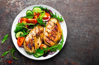Izgara tavuk göğsü. Kızarmış tavuk fileto ve taze sebze salatası domates, salatalık ve roka yaprakları. Salatalı tavuk eti. Sağlıklı yiyecekler. Düz yatıyordu. Üst Manzara. Koyu arkaplan