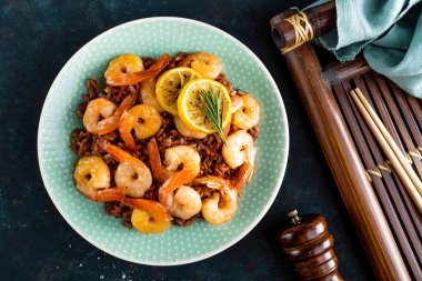 Karides ızgara kavrulmuş ve plaka üzerinde kahverengi pirinç haşlanmış. Izgara karides, karides pirinç. Deniz ürünleri. Asya mutfağı. Üstten Görünüm. Koyu arka plan