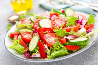 Domates, salatalık, tatlı biber ve susam ile taze sebze salatası. Beyaz tabakta sebze salatası