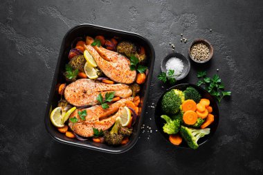 Somon balığı. Siyah arka planda fırında somon balığı bifteği, brokoli, havuç ve soğan.