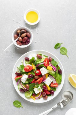Beyaz tabakta yeşil zeytinli Yunan salatası ve feta satrancı.