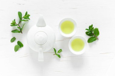 Yeşil nane çayı, fincanlarda taze yapraklar, beyaz ahşap masada çaydanlık, sağlıklı ısınma içeceği, antioksidan içeceği, üst görüş.