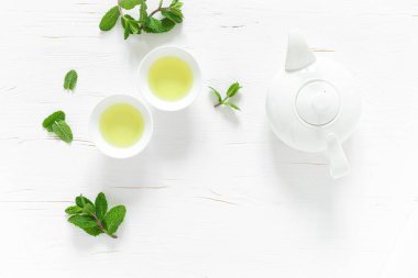 Yeşil nane çayı, fincanlarda taze yapraklar, beyaz ahşap masada çaydanlık, sağlıklı ısınma içeceği, antioksidan içeceği, üst görüş.