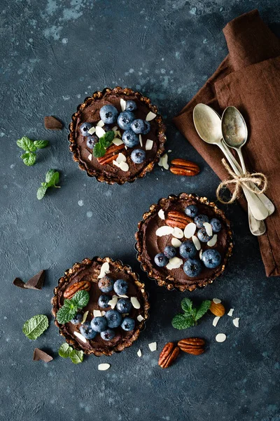 Healthy raw vegan dessert dates tartlets with chocolate cream of cashew, decorated with almond, pecan nuts and fresh blueberry