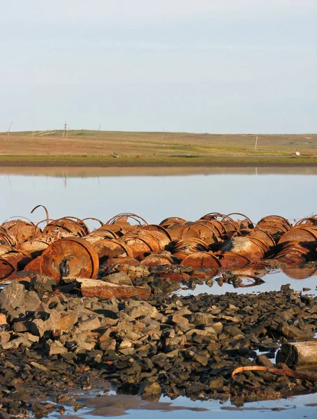 Kuzey Kutbu gölünün arka planında eski paslı demir variller. Çevre felaketi