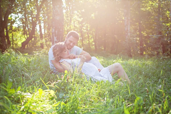 Мужчина и беременная жена отдыхают на траве — стоковое фото