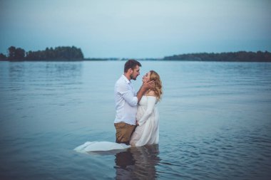 Yakışıklı delikanlı ve onun hamile eşi göl su ayakta ve öpüşme 