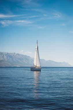 Denizde yelken açan yat, dağların arka planında.