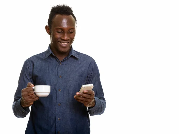 年轻快乐的非洲黑人男人一边微笑着 一边拿着咖啡杯 一边用手机 — 图库照片