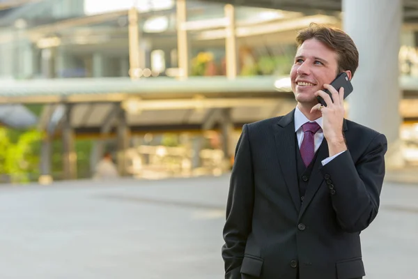Счастливый Вдумчивый Бизнесмен Улыбается Разговаривает Мобильному Телефону Перед Современным Зданием — стоковое фото