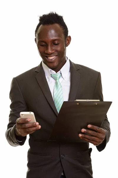 Junger Glücklicher Afrikanischer Geschäftsmann Lächelt Und Benutzt Handy Während Klemmbrett lizenzfreie Stockbilder