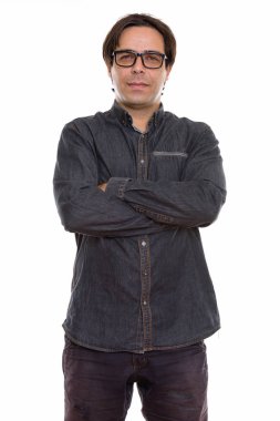 Stüdyoda genç İranlı adam ayakta ve kollarını kavuşturmuş gözlük takıyor.