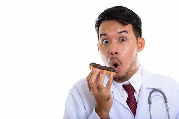Studio Strzał Młody Azji Człowiek Lekarz Jedzenie Pączka Podczas Patrząc — Zdjęcie stockowe