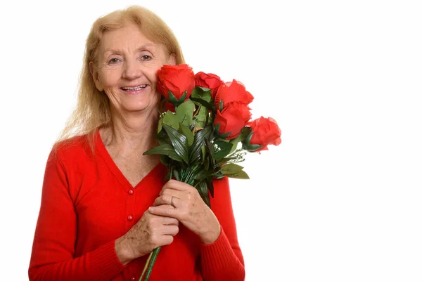 Studio Záběr Šťastné Starší Ženy Usmívá Drží Červené Růže Blízkosti — Stock fotografie