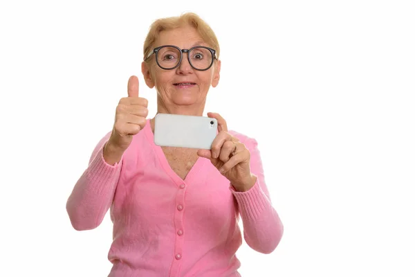 快乐的老书呆子女人一边微笑着一边用手机拍照和放下大拇指 — 图库照片