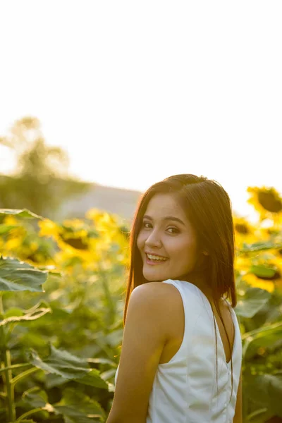 Jeune femme asiatique heureuse souriant et regardant en arrière dans le domaine de — Photo