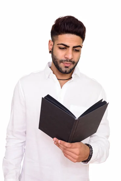 Studio shot of young handsome Indian man reading isolated agains — Stock Photo, Image