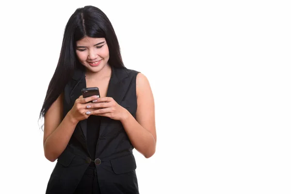 Studio shot of young happy Asian woman smiling while using mobil — Stock Photo, Image