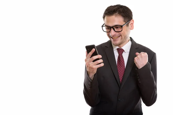 Студийный снимок счастливого молодого бизнесмена, улыбающегося при использовании мобиля — стоковое фото