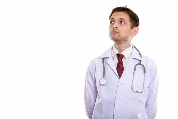 Studio shot of young man doctor thinking while looking up — Stock Photo, Image