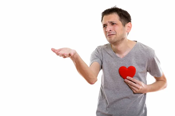 Studio shot de jeune homme triste donnant la main avec le cœur rouge sur la poitrine — Photo