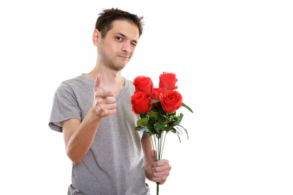 Studio shot of young man holding red roses while pointing at cam — Stock Photo, Image