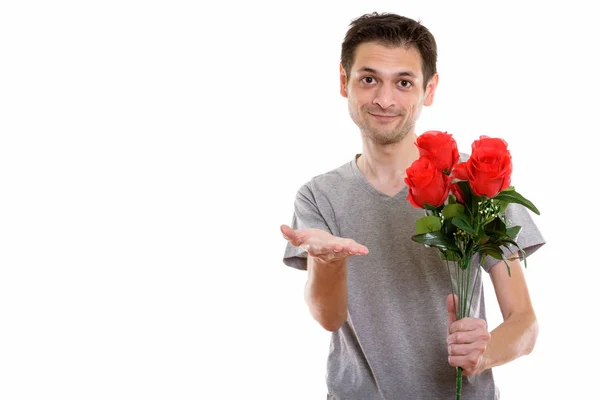 Studio shot di giovane uomo che tiene rose rosse mentre dà la mano rea — Foto Stock