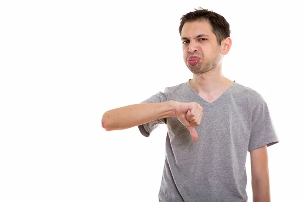 Студійний знімок молодого чоловіка, який дає великий палець вниз, приклеюючи язик — стокове фото