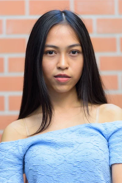 Faccia di giovane bella ragazza asiatica adolescente contro muro di mattoni — Foto Stock