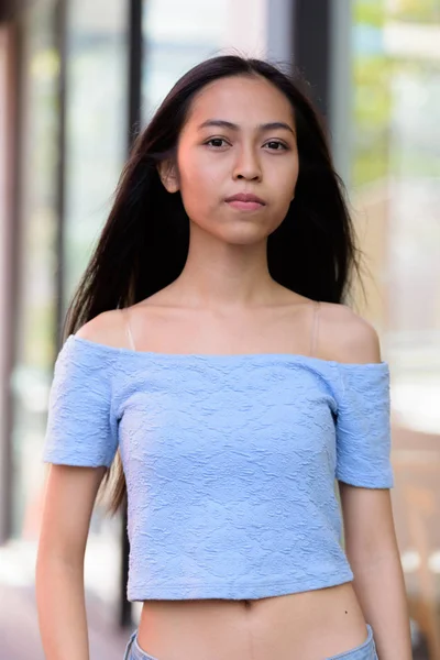 Mooie Aziatische tiener meisje lopen buiten koffie winkel met glazen ramen — Stockfoto