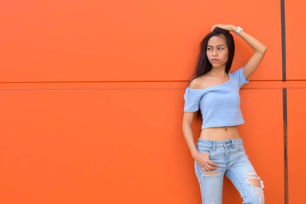 Молодих красивих азіатських Дівчинка-підліток думає з рук на голову при Пізанської помаранчеві стіни пофарбовані — стокове фото