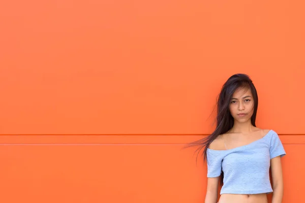 Молодий красива Азіатська Дівчинка-підліток притулившись помаранчеві стіни пофарбовані — стокове фото