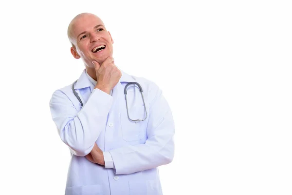 Estudio de tiro de joven calvo feliz doctor sonriendo mientras piensa —  Fotos de Stock