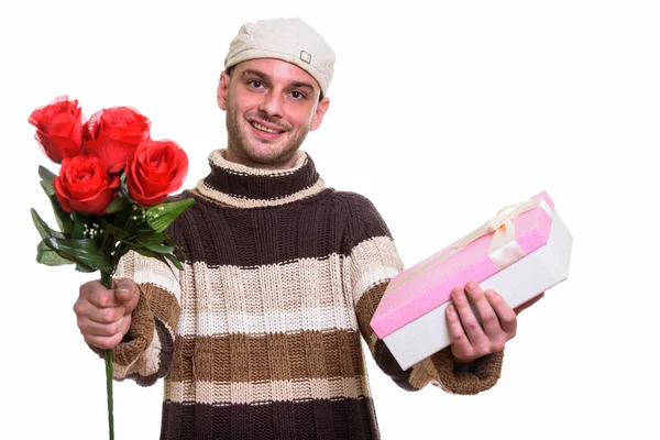 Estudio de tiro de joven feliz hombre sonriendo mientras que da rosas rojas un — Foto de Stock