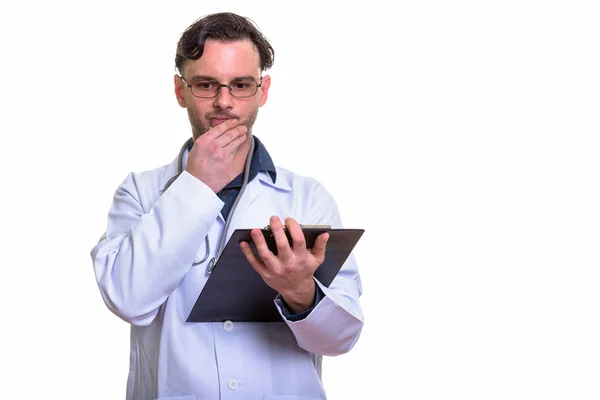 Studio shot of young man doctor holding clipboard while thinking — Stock Photo, Image