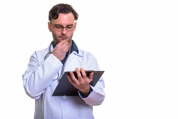 Estudio de la toma de un joven doctor leyendo en el portapapeles mientras piensa —  Fotos de Stock